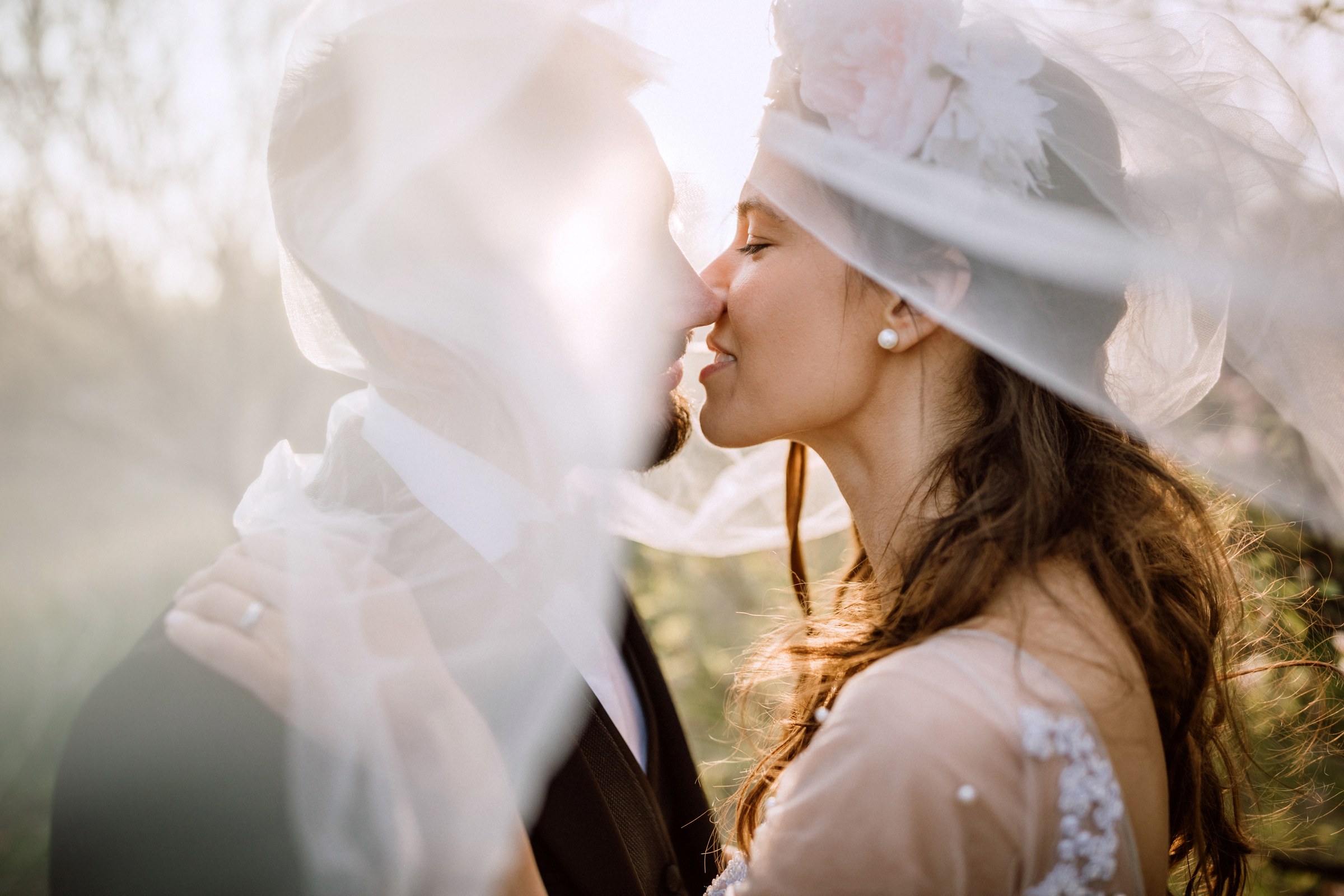 Bride and groom sharing a kiss beneath a flowing veil in golden Scottish light